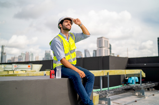 Caucasian professional engineer or technician sit on terrace of construction with relax after work and look around with happiness for success of the project.