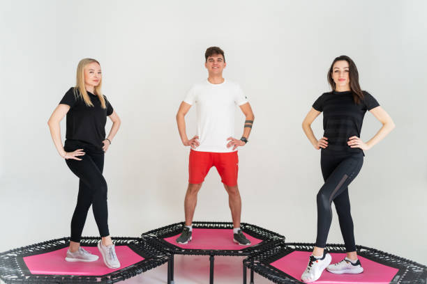 Three adorable fitness people In sportswear jumping on sport trampoline White background stock photo