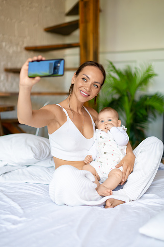 Young mother with her newborn daughter during an online video chat with her father. A woman shows their daughter to dad, smiles and communicates with her husband.
