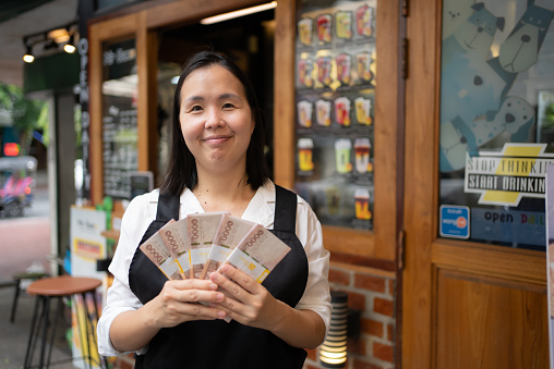 Cheerful young female business owner smiles while holding money