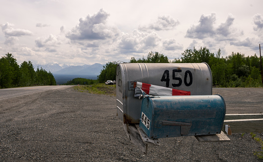 An image of an old rusted rural mailbox on the side of a gravel road.