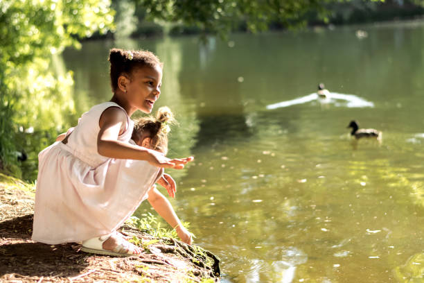 Happy caucasian and African-American girls watching birds on a pond on a summer day in the park.Summer,diversity concept