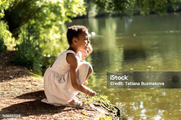 Happy caucasian and African-American girls watching birds on a pond on a summer day in the park.Summer,diversity concept.