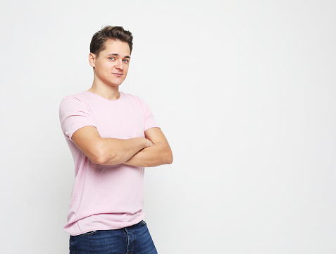 Young handsome man wearing pink t-shirt crossing hands and look at camera over white background