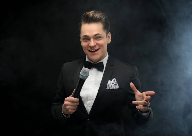 Stylish young man in a tuxedo holding a microphone, posing against a dark background with smoke stock photo