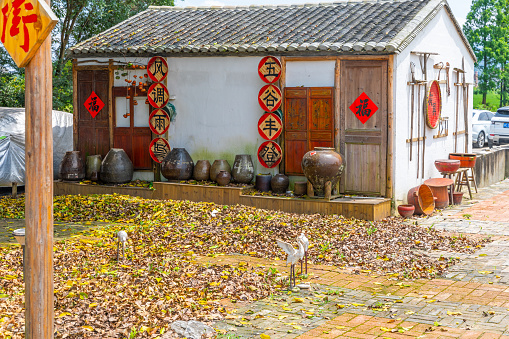 Wenzhou, Zhejiang Province, China - July 19, 2022:  A traditional building exterior. The construction has diverse agricultural tools hanging from the lateral wall. Chinese characters and water containers are seen in the front. No people in the scene.