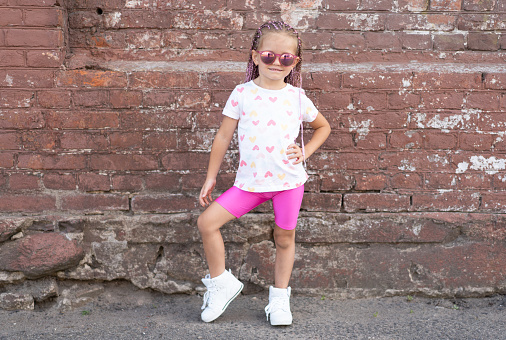 Fashion kid concept - stylish little girl child wearing bright clothes and sunglasses against the colorful wall