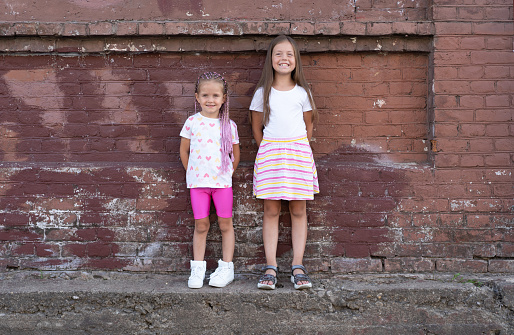 Fashion kid concept - stylish girls child wearing bright clothes against the colorful wall. Portrait of two cute sisters