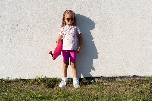 Fashion child girl in sunglasses with pink skateboard in the city
