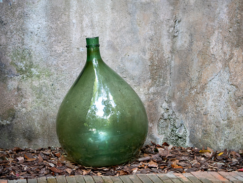 Antique demijohn in garden  grey background