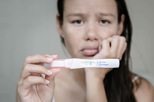 A unhappy depressed woman with a close up negative pregnancy test result.