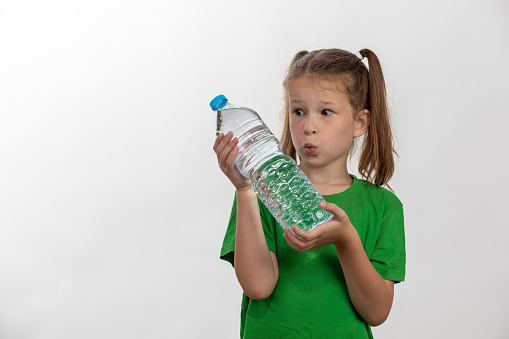 Little girl holding plastic water bottle. Hydrate and stay healty. Looking at bottle.