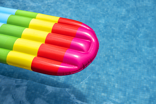 Multicolored air mattress floating in the blue water of a swimming pool.