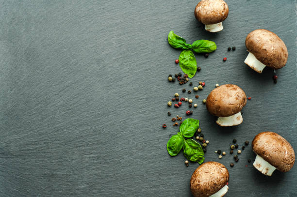 ingredients for cooking: champignon mushrooms, green basil, a mix of fragrant spices peppercorns on a black background, top view, layout, space for text