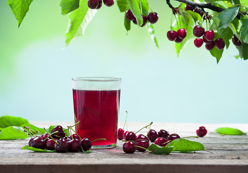 A glass of fresh cherry juice. Freshly squeezed cherry juice and cherries on the garden table