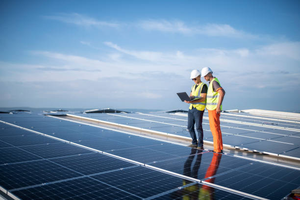 Team of engineers using technology while installing solar panels on a roof of warehouse. stock photo