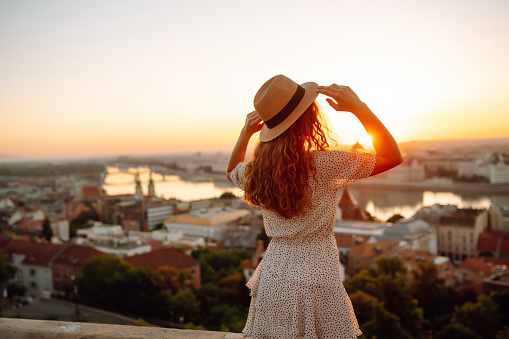 Portrait of a young woman in a hat at sunset enjoying the view of the city. Lifestyle, travel, tourism, nature, active life.