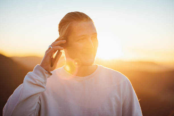 Happy Young man standing during sunset while having a phone call with his mobile phone. Millennial Generation Real People Urban Lifestyle.