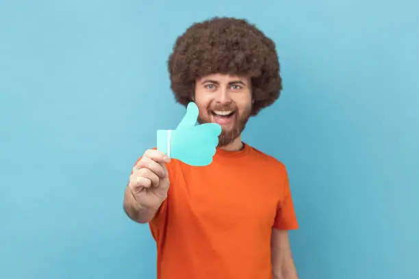 Photo of Man showing thumbs up blue paper sign, liking and recommending posts in social networks.