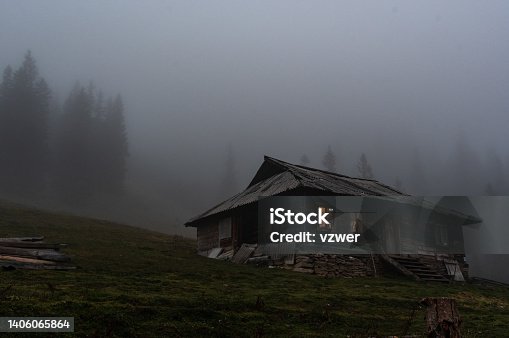 istock Lonely hut in the forest. Lonely wooden house in the mountains. Gloomy house with luminous windows. 1406065864