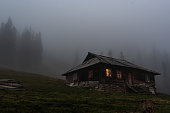 istock Lonely hut in the forest. Lonely wooden house in the mountains. Gloomy house with luminous windows. 1406065864