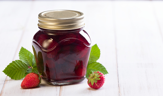 Jar of strawberry jam on white table.