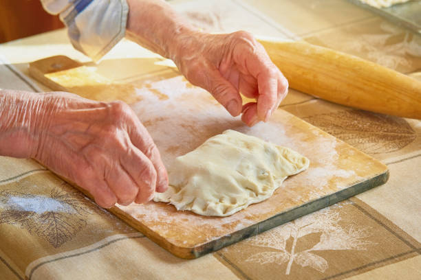 istock An elderly woman sculpts pies stuffed with dough on a cutting board. 1406072592