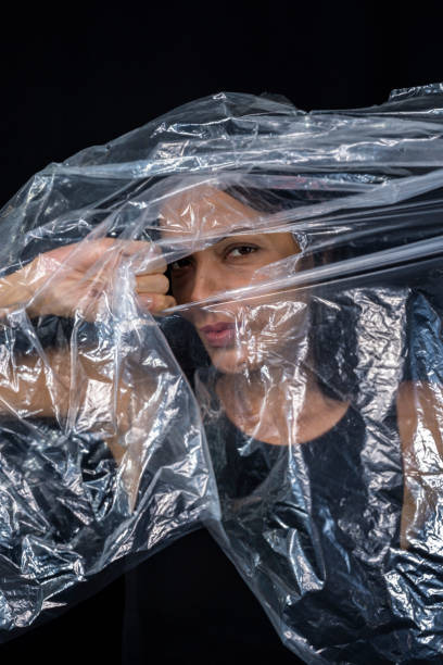istock Model portrait with clear plastic in front of her face against black background. 1406077142
