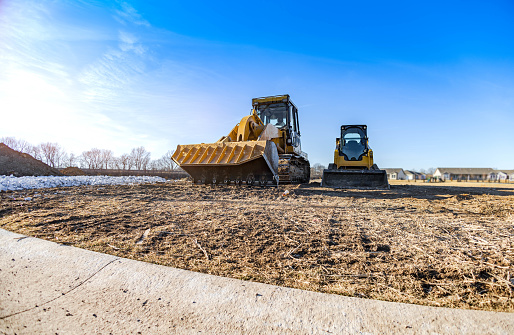 Track bulldozer, earth-moving equipment at the construction site with the bright blue sky background. Land clearing, grading, ground excavation, foundation digging of the large job of the new residential building.