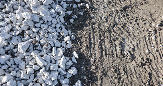 Top view, pile of white and gray stone on the soil ground with natural sunlight. Abstract two tone of small rocks pattern. Mix element for new building foundation at construction site. Rough texture.
