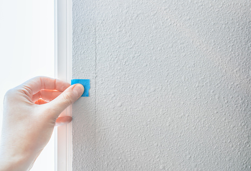 A person's hand sticks a blue sticker on paint cracked wall, checking the quality of house defect construction. Interior inspection of the mark, material and surface for fix and repair. Home Improvement concept.