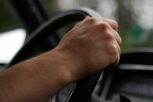 Defocus male hand holding steering wheel. A man's hand handle steering wheel car for driving. Traffic jam, driving car on highway, close up of hands on steering wheel. Closeup. Out of focus.