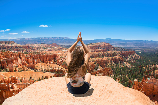 Woman practicing yoga in nature. Carefree girl sitting on top of the mountain  meditating. Inspiration Point ,Bryce Canyon National Park, Utah, USA