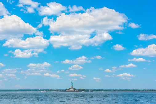 The Statue of Liberty is seen at a distance under a blue, cloudy sky.