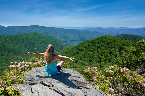 Woman sitting with outstretched arms in summer mountain scenery. Joyful woman on hiking trip relaxing looking at beautiful mountain view. Blue Ridge Parkway, Near Asheville,North Carolina, USA.