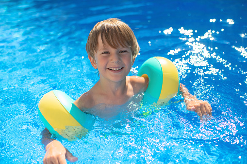 Portrait of a strong and confident little boy practicing swimming at indoors swimming pool. The boy aged 8 is smiling out of the pool into the camera. 