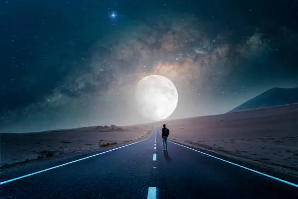 Photo of road to the moon in the desert at night with silhouette of a person