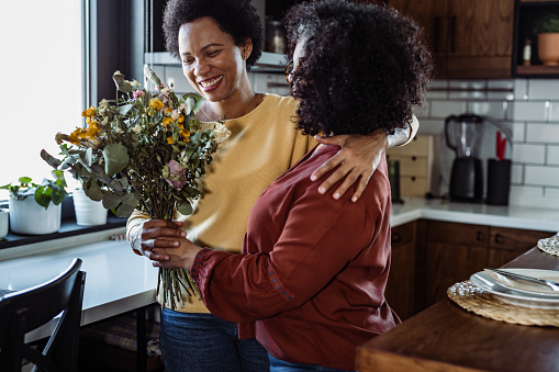 Mid adult woman giving a bouquet of flowers to her wife in the kitchen