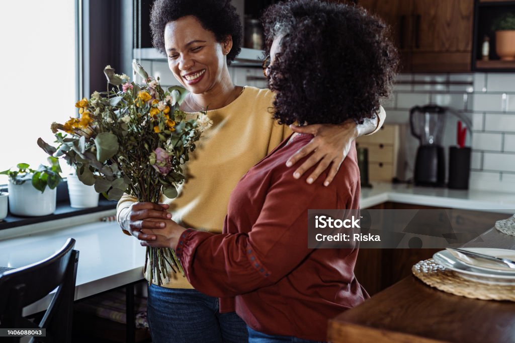 You deserved it. I love you Mid adult woman giving a bouquet of flowers to her wife in the kitchen Flower Stock Photo