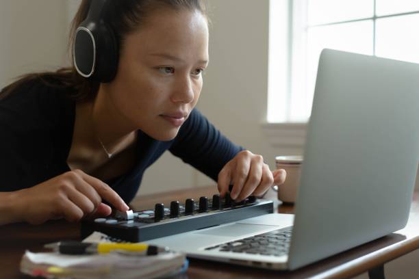 una mujer con auriculares y usando su computadora en casa. hacer música y editar fotos. - filipino ethnicity audio fotografías e imágenes de stock