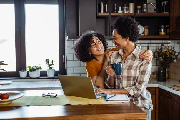 Two mature women in love Mid aged lesbian couple drinking coffee in the kitchen. One of them is embracing the other one. gay dinner table stock pictures, royalty-free photos & images