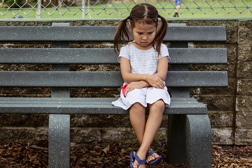 Unhappy little girl sitting alone outside at school.