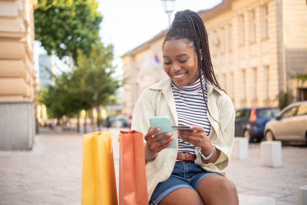 幸せな女性は、オンラインで買い物をし、街で楽しむ - spending money adult african ethnicity bag ストックフォトと画像