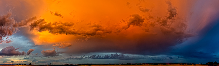 Panoramic photo of a departing thundercloud illuminated orange by the light of the setting sun