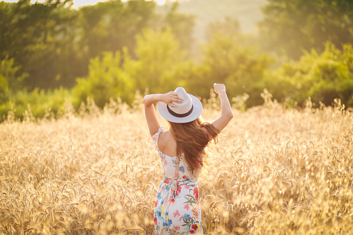 happy young woman in wheat field by sunset