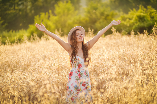 happy young woman in wheat field by sunset