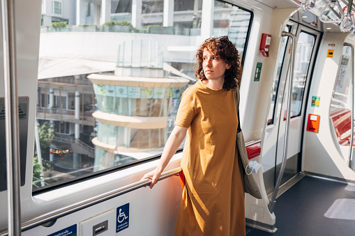 A young woman with curly hair riding the light rail and looking out the window.
