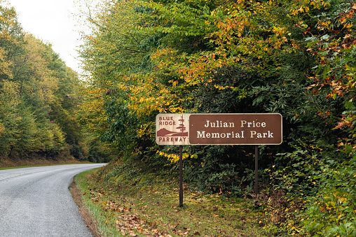 Blowing Rock, USA - October 6, 2021: Colorful yellow foliage in fall season in North Carolina Blue Ridge mountains paved road parkway and sign for Julian Price Memorial Park