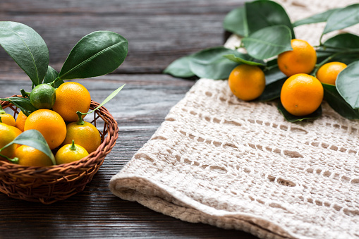 Citrus Calamondin with leaves in basket on linen napkin on wooden board