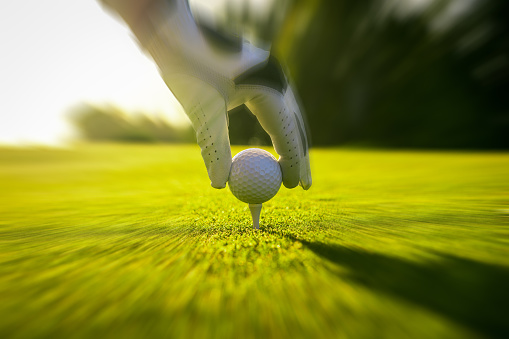 Closeup of golfer wearing glove placing golf ball on tee at golf course